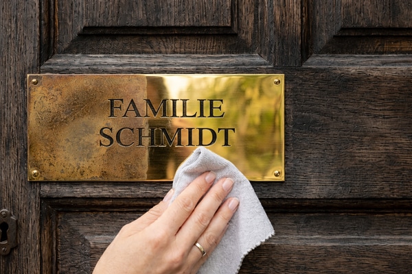Messingschild an einer Haustür wird mit einem Tuch gereinigt – Pflege eines gravierten Türschilds